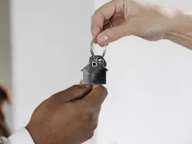 a person handing a key with house pendant to another person